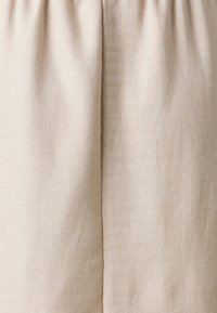 Jupe en lin beige avec taille froncée, présentant un tissu texturé et doux. Le design comprend une silhouette droite avec des détails de couture minimaux.