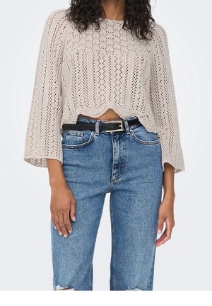 Beige knitted sweater with open lace pattern, cropped design, and bell sleeves, paired with high-waisted blue denim jeans and a black belt.