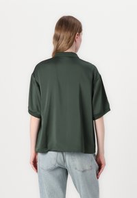 Grønn sateng skjorte med korte ermer og krage, med en glatt tekstur og en avslappet passform, parret med lyseblå høytlivsjeans.