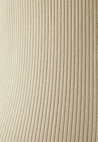 Beige ribbad tyg som har vertikala linjer av varierande bredd, med en slät yta och subtil lyster, som betonar elasticitet.