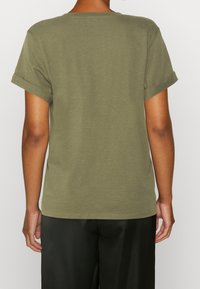 Camiseta de algodón verde oliva con mangas cortas enrolladas, cuello redondo clásico y corte recto. Textura suave sin patrones visibles.