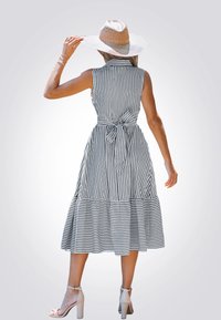 Vestito a righe con gonna a strati, tessuto leggero, colletto e cintura in vita; modella che indossa un cappello a tesa larga e tacchi, vista da dietro.