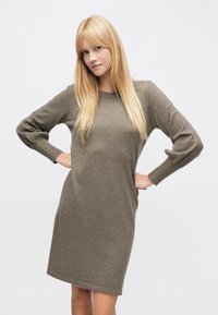 Sukienka z długim rękawem, sięgająca do kolan, wykonana z miękkiej oliwkowozielonej tkaniny o luźnym kroju i ściągaczowych mankietach. Bezszwowa konstrukcja bez wzorów.