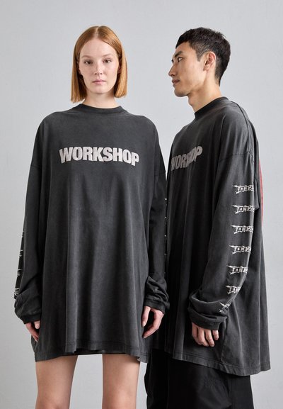 Černé oversize trička s dlouhým rukávem, na přední straně s nápisem "WORKSHOP", vyrobené z měkkého, texturovaného materiálu a s grafickými akcenty na rukávech.