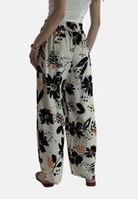 Brede broekspijpen van een lichte stof met een bloemenpatroon met zwarte en oranje bloemen op een crème achtergrond, elastische tailleband, zonder zakken.