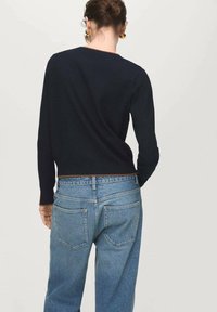 Maglione corto blu navy con scollatura rotonda, indossato sopra jeans a vita alta azzurri. Texture liscia con linee semplici e pulite.
