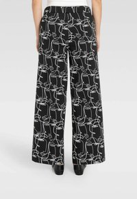 Pantaloni neri a gamba larga con un motivo a disegno astratto bianco. Il tessuto ha una texture liscia e una vita aderente sul retro.
