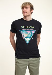 Svart t-shirt med kort ärm som har en färgglad grafisk design med texten "St. Lucia", triangelform, palmer och en illustration av en segelbåt.