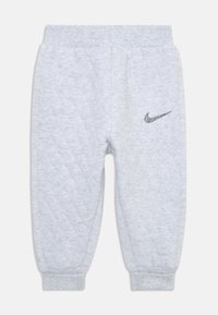 Šedé prešívané tepláky s manžetami na členkoch a elastickým pásom. Obsahujú čierne logo Nike na ľavom stehne. Mäkká textúra látky.