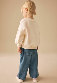 Pull-over couleur crème avec manches bouffantes et poignets côtelés, associé à un jean large en denim bleu clair. Design simple, texture douce.