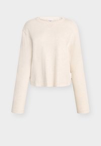 Haut à manches longues court couleur beige clair, en tissu doux, avec un col légèrement évasé et une texture côtelée, orné d'une étiquette sur le côté.