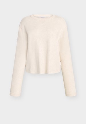 Top a maniche lunghe color beige chiaro, corto, realizzato in tessuto morbido, con scollo leggermente svasato e texture a coste, con etichetta laterale.