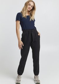 Navy short-sleeve t-shirt paired with black high-waisted jogger pants with a belt. Model wears gray sneakers; fabric appears soft and lightweight.