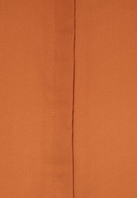 Oranžová tkanina s texturou a matným povrchem, s výrazným švem uprostřed a jemnými odstíny tónů.