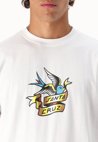 Camiseta de algodón blanca con un diseño colorido estilo tatuaje que presenta un pájaro azul y una cinta marrón con el texto "SANTA CRUZ".