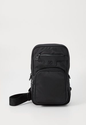 Černá kompaktní crossbody taška s nastavitelným popruhem, dvěma kapsami na zip a vyraženým logem HUGO na přední kapse.