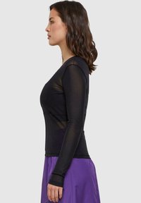 Schwarzes longsleeve Oberteil mit transparenten Einsätzen, taillierter Silhouette und Rundhalsausschnitt, kombiniert mit einem lila Rock.