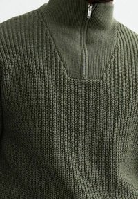 Maglione lavorato a maglia di colore verde scuro con colletto alto e zip a metà. Presenta un motivo a coste testurizzato e un collo a V distintivo.
