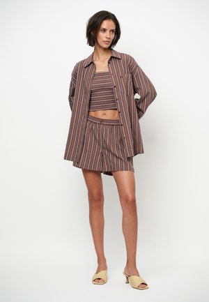 Vrouw draagt een overshirt met verticale bruin-witte strepen, een bijpassende cropped top en korte broek, gecombineerd met beige gevlochten sandalen met hak.