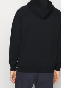Felpa nera con cappuccio, dotata di polsini e orlo a costine, caratterizzata da una texture liscia e un design minimalista, vista da dietro.