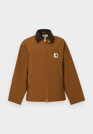 Rudas Carhartt švarkas su tamsiu kordurojų apykakle, priekinio užtrauktuko, krūtinės kišenės su užtrauktuku ir priekinio logotipo lopeliu, pateiktas ant balto fono.