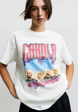 Junge Frau trägt ein weißes T-Shirt mit vier Porträts einer blonden Frau unter dem Schriftzug „Cardi B“ und dem Slogan „Am I the drama?".