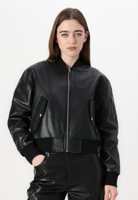 Bomber jacket in pelle nera con chiusura a zip, polsini a coste e due tasche laterali. Texture liscia con design strutturato e orlo aderente.