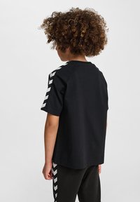 T-shirt nera a maniche corte, con strisce a zigzag bianche sulle spalle. Taglio dritto, realizzata in tessuto leggero.