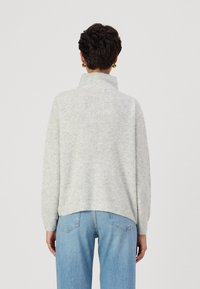 Light grey sweater with a ribbed texture, high collar, and dropped shoulders, paired with light blue jeans featuring a classic five-pocket design.