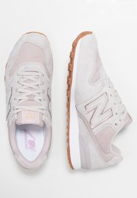 Helle graue Wildleder-Sneaker mit einem strukturierten Design, ausgestattet mit einer weißen Zwischensohle und einer Sohle aus Gummi. Akzentuiert mit einem pinken Logo und Schnürsenkeln.