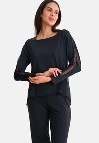 T-shirt noir à manches longues avec un col bateau et des détails en dentelle le long des manches, fabriqué en tissu lisse. Assorti à un pantalon foncé.