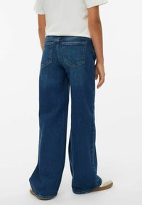 Jean large bleus en denim, avec poches arrière, coupe droite et une légère décoloration, associés à des sneakers de couleur claire.