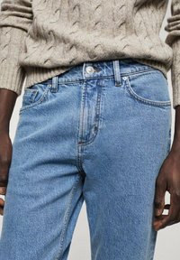 Jeans de mezclilla azul claro con corte de pierna recta, con cierre de botones, cinco bolsillos y un sutil desvanecimiento que aporta textura.