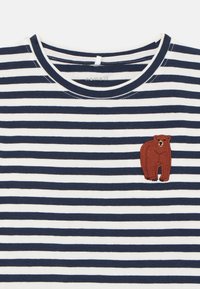 Marineblå og hvite stripete crew-neck skjorte med en liten brodert brun bjørn på øvre venstre brystområde.