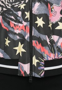 Chaqueta bomber con cremallera, base negra, patrones de estrellas en rosa vibrante y amarillo, texturas de malla y puños acanalados negros que contrastan.