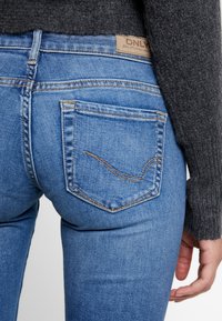 Jeans de mezclilla azul con un diseño ajustado, que presentan un lavado claro, bolsillos traseros y una etiqueta beige con "ONLY" en la cintura.