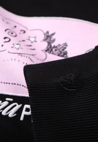 Pull-over noir avec un motif rose comportant des tourbillons et des étoiles. Le texte indique « Mia P » en blanc. Poignets côtelés avec un petit logo en accent.