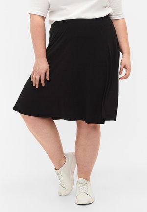 Jupe noire en A fabriquée dans un tissu doux, dotée d'une taille texturée et d'un ourlet fluide. Portée avec des baskets blanches pour un look décontracté.