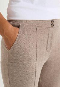 Pantalons à motif pied-de-poule en beige clair avec une texture lisse, dotés de poches latérales et de deux boutons avant pour la fermeture.