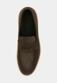 Zapato marrón de cuero tipo slip-on con una correa elevada en el empeine, puntera redondeada y suela de goma color crema. Textura suave en toda la superficie.