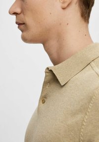 Beige poloshirt met een ribgebreide kraag, knoopsluiting en een zachte textuur. De stof lijkt lichtjes gestructureerd met zichtbare stiksels.