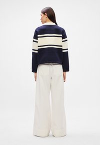 Jūrinės tamsiai mėlynos ir kreminės juostelės trumpas megztinis, derinamas su plačius kojas turinčiomis of-white kelnėmis, turinčiomis kišenes ir lygiu paviršiumi.