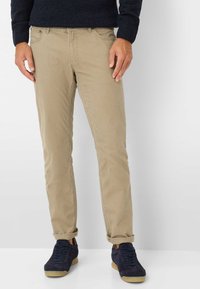 Beige Baumwollchinos mit schmaler Passform, seitlichen Taschen, Gürtelschlaufen und umgeschlagenen Bündchen, kombiniert mit navyblauen Wildledersneakern.