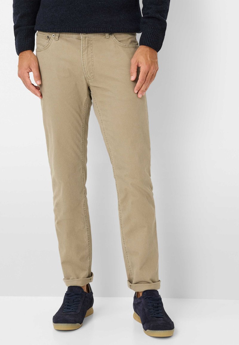 Beige Baumwollchinos mit schmaler Passform, seitlichen Taschen, Gürtelschlaufen und umgeschlagenen Bündchen, kombiniert mit navyblauen Wildledersneakern.