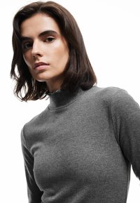 Grauer gerippter Pullover mit hohem Kragen und weichem Material. Verfügt über lange Ärmel und eine taillierte Passform, wodurch ein minimalistischer Stil hervorgehoben wird.