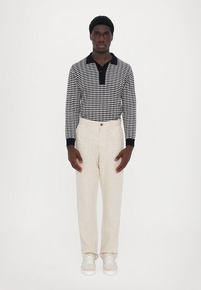 Striped navy and white long-sleeve polo shirt with a black collar, paired with light beige linen trousers and gray sneakers.