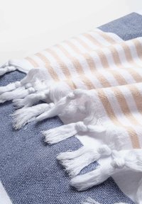 Tessuto di cotone con strisce bianche e pesche, con frange decorative bianche; poggia su uno sfondo blu texturizzato.