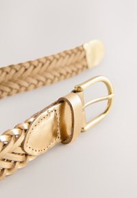 Cinturón trenzado de cuero color caramelo con hebilla y punta doradas, mostrado en primer plano sobre un fondo claro.