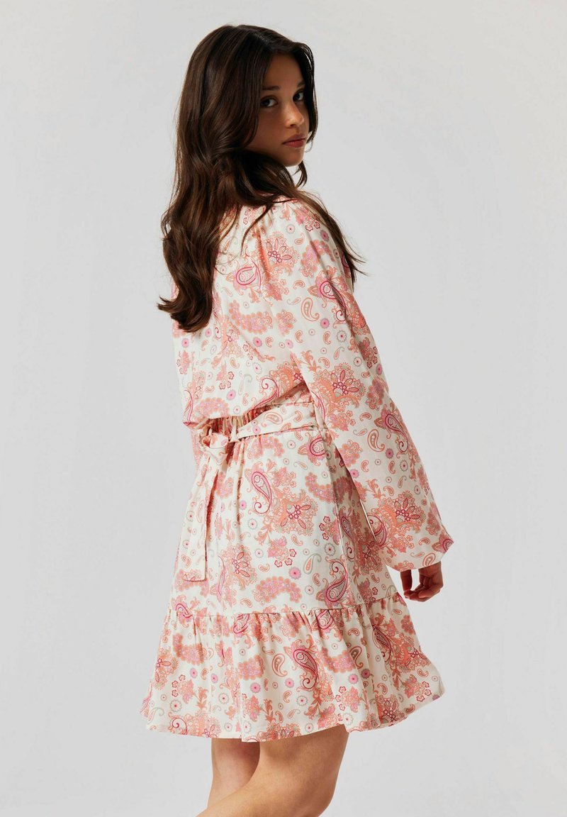 Robe à motifs floraux en rose clair et blanc, avec des manches longues, une taille cintrée et un ourlet festonné. Une ceinture nouée accentue la silhouette.