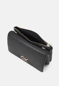 Schwarze Leder-Clutch mit einem Rei�ßverschluss, die auf der Vorderseite mit einem goldenen Logo-Detail versehen ist und ein glattes Innenfutter hat.